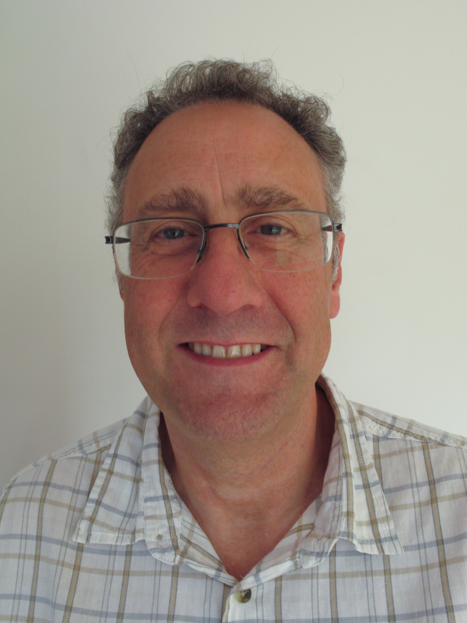 Image shows a picture of Carl Hodge. He is smiling towards camera and wears a checked shirt and glasses.