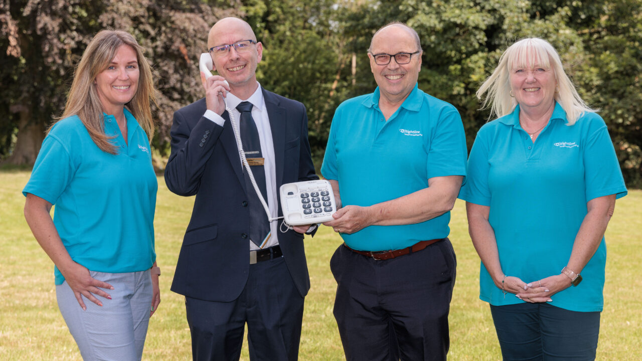 Image shows Miller Homes Development Sales Manager Andy Brooks with Sightline Marketing Manager Rebecca Billington, Charity Director Ian Edwards and Services Manager Andrea Allinson. Andy is holding a phone up to his right ear and everyone is smiling towards the camera.