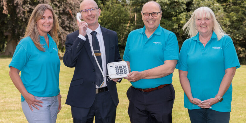 Image shows Miller Homes Development Sales Manager Andy Brooks with Sightline Marketing Manager Rebecca Billington, Charity Director Ian Edwards and Services Manager Andrea Allinson. Andy is holding a phone up to his right ear and everyone is smiling towards the camera.