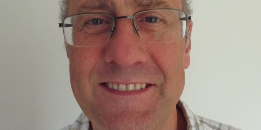 Image shows a picture of Carl Hodge. He is smiling towards camera and wears a checked shirt and glasses.